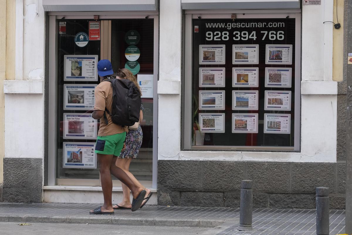 Una pareja camina por delante de una agencia inmobiliaria en Canarias.