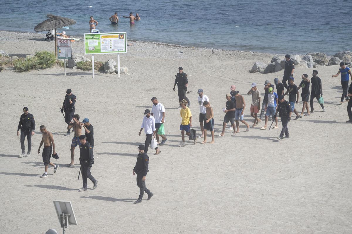 Varios migrantes, el pasado fin de semana en una playa de Ceuta custodiados por policías nacionales.