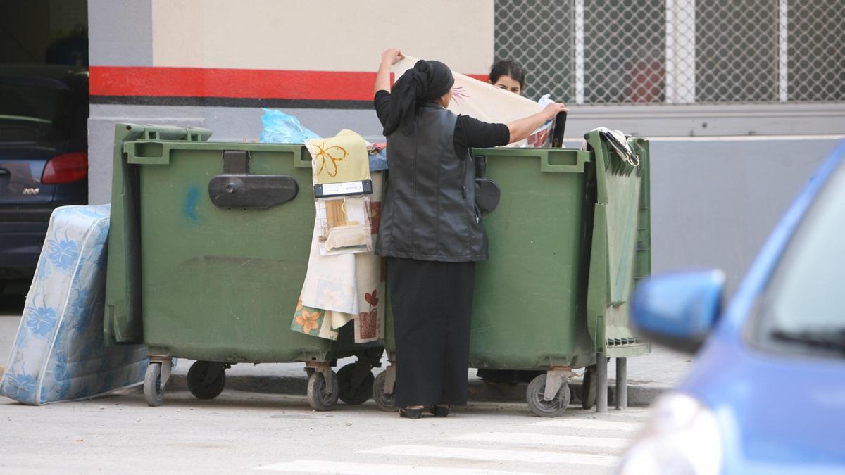 Dos personas rebuscan entre la basura de un contenedor, en una calle de Xàtiva.