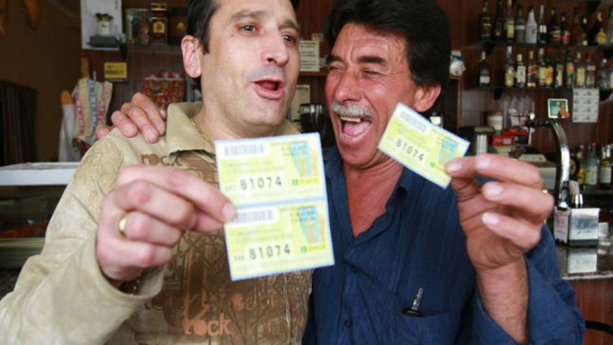 Pedro Antonio López González, dueño del bar Los Franceses, muestra dos cupones premiados mientras se abraza con otro afortunado que no puede disimular su enorme alegría por el dinero ganado con otro cupón