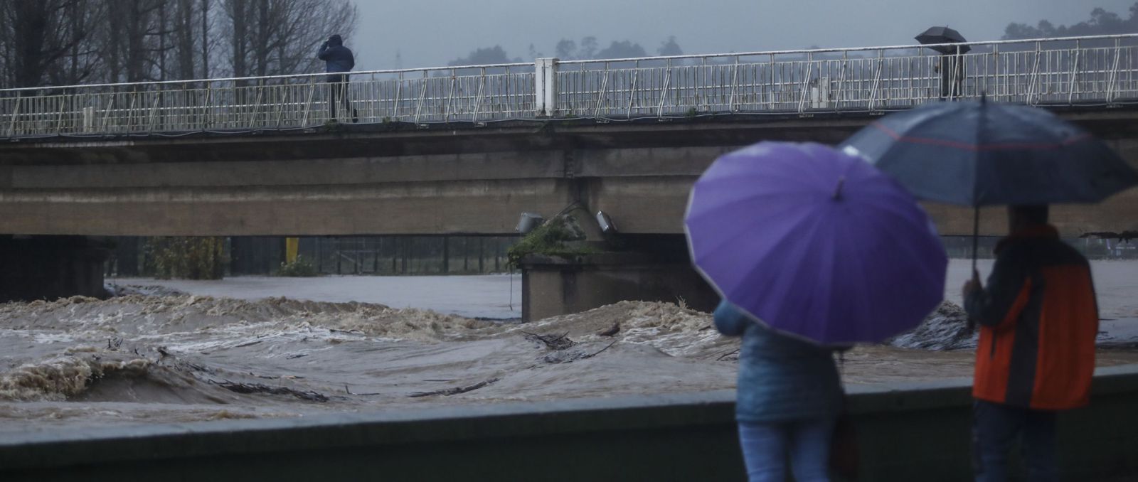 Dos vecinos observan el salvaje discurrir del río por Arriondas ayer por la tarde. | Luisma Murias