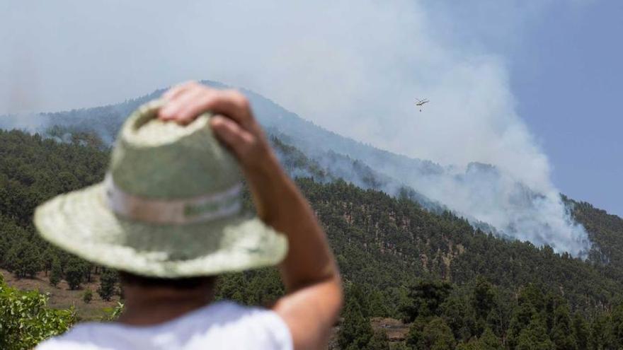 Una residente de La Palma observa cómo un helicóptero arroja agua sobre el fuego.