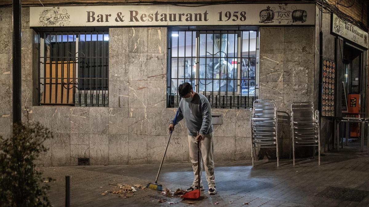 El propietario de un bar cercano a la plaza de la Trinitat Vella barre su parcela, la noche del martes