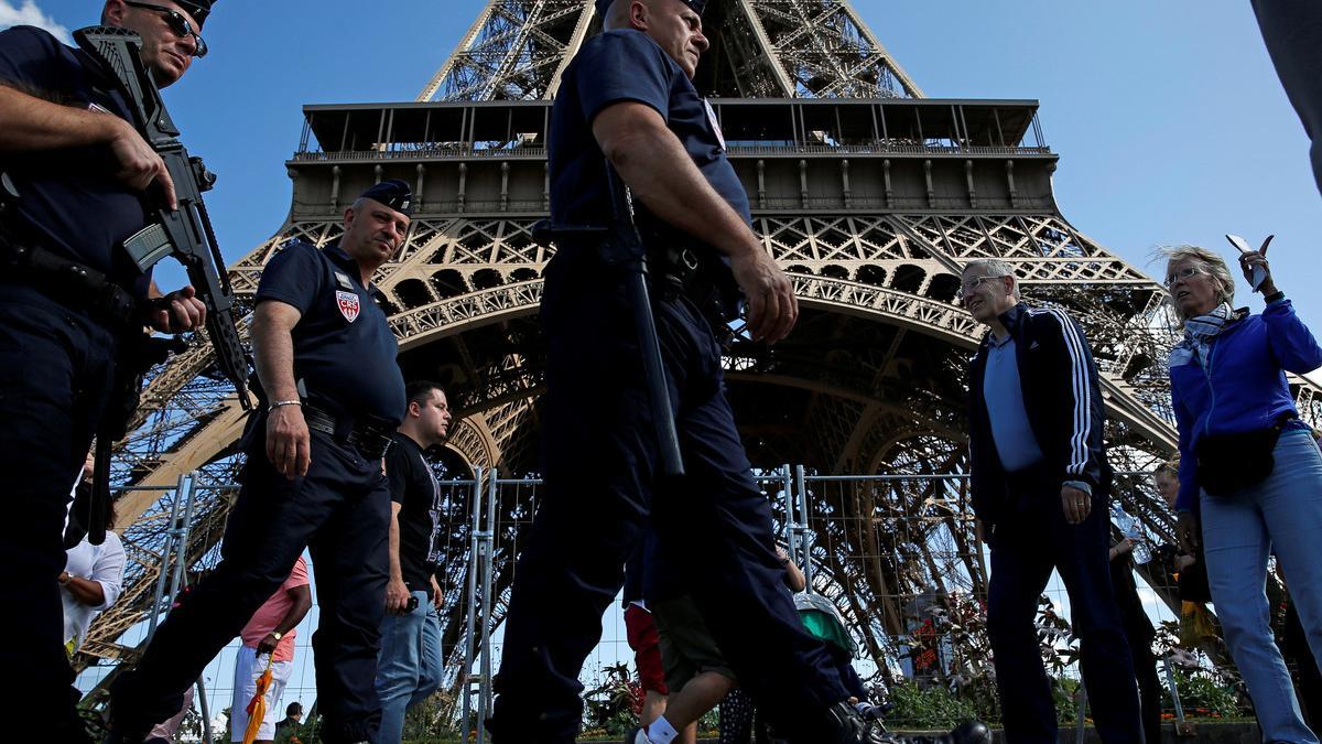French CRS policemen patrol as tourists walk past in front of the Eiffel Tower in Paris
