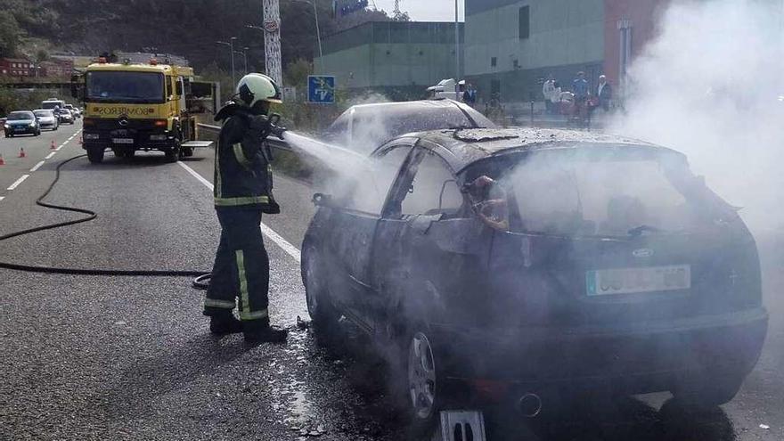 Un bombero acaba de apagar el fuego en el coche, ayer, en El Entrego.