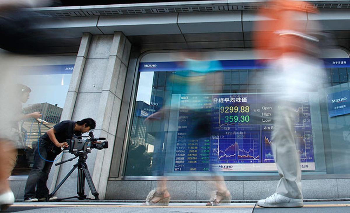 Un càmera de televisió grava un panell amb l’índex Nikkei, en un carrer de Tòquio.