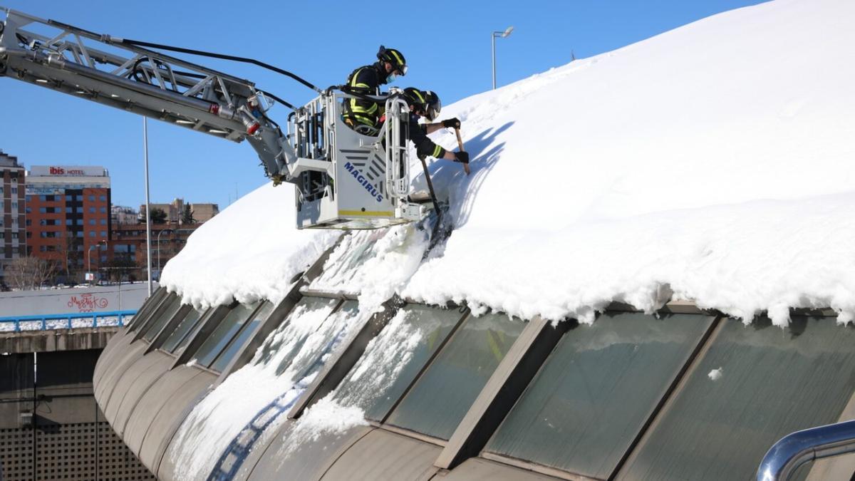 Operarios municipales retiran nieve de un tejado subidos a una grúa.