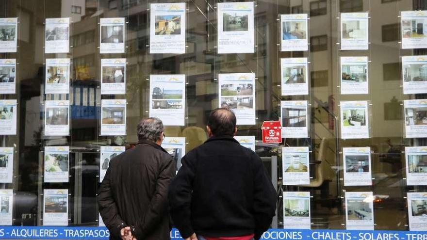 Dos hombres observan los anuncios de pisos en una inmobiliaria.