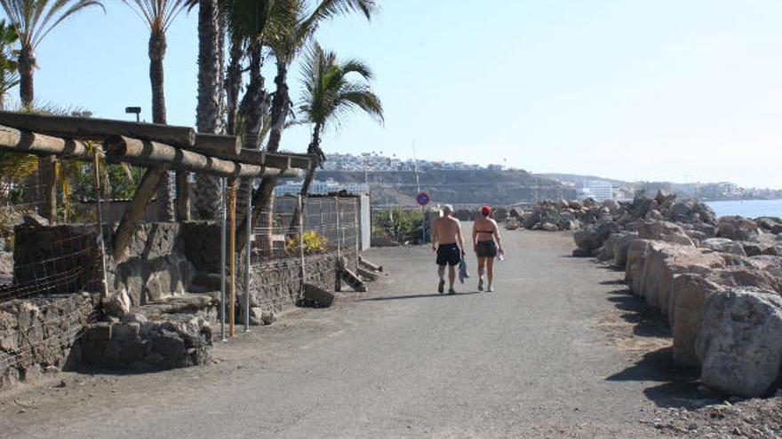 Dos turistas caminan por el paseo marítimo de Anfi del Mar en medio del deterioro de la zona.