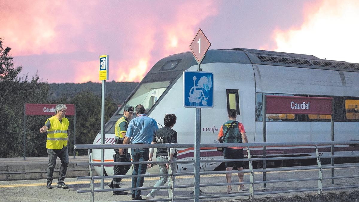 La Guardia Civil vigila la evacuación del tren afectado por el incendio de Bejís (las llamas se ven al fondo), en la estación de Caudiel.