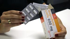 Una mujer saca varias pastillas de ibuprofeno de su caja.
