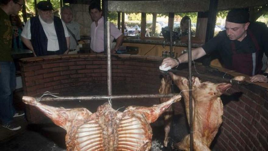 Alejandro Platas da la vuelta al cordero ante la antenta mirada de George R. R. Martin, detrás, junto al concejal avilesino Román Antonio Álvarez y José Manuel Álvarez, propietario del local.  / mara villamuza