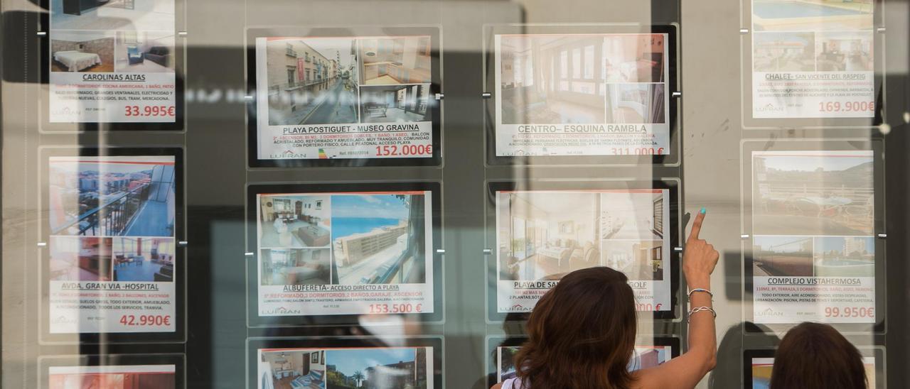 Una pareja consulta anuncios de pisos en venta en una agencia inmobiliaria de Alicante