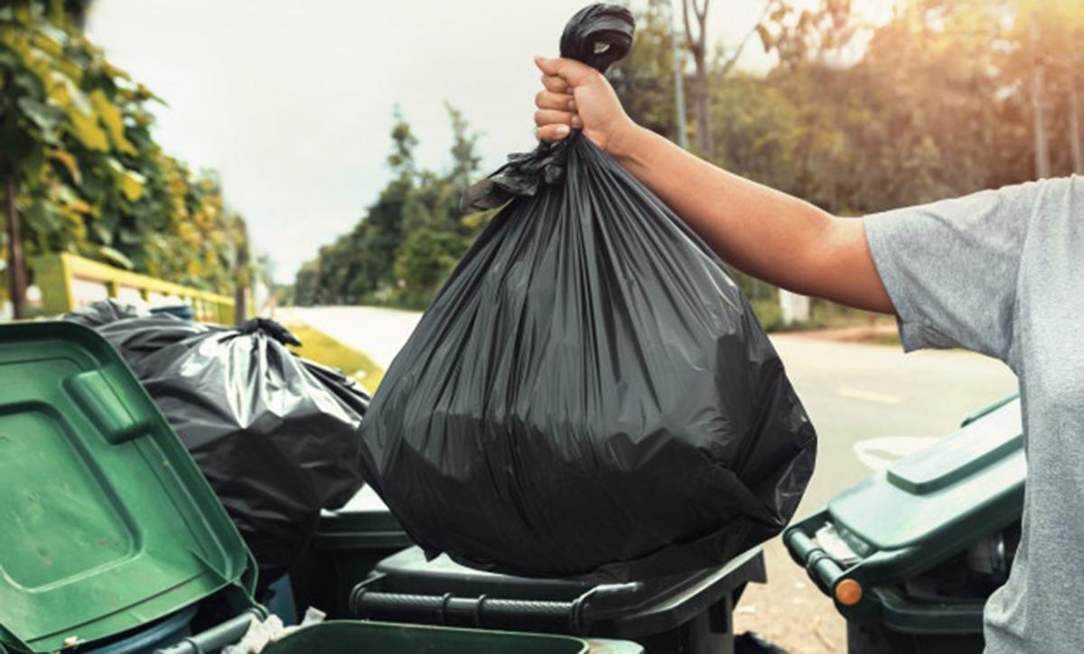 Un hombre arroja una bolsa de basura al contenedor.