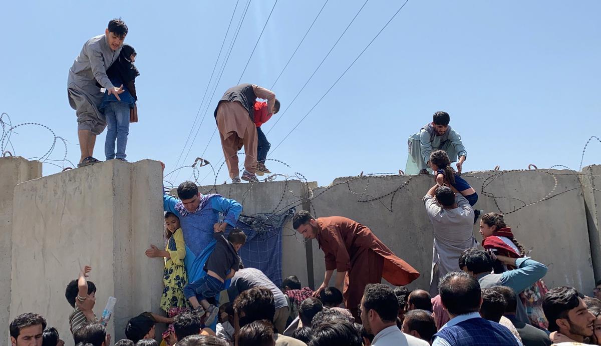 Las personas luchan por cruzar el muro fronterizo del aeropuerto internacional Hamid Karzai para huir del país.