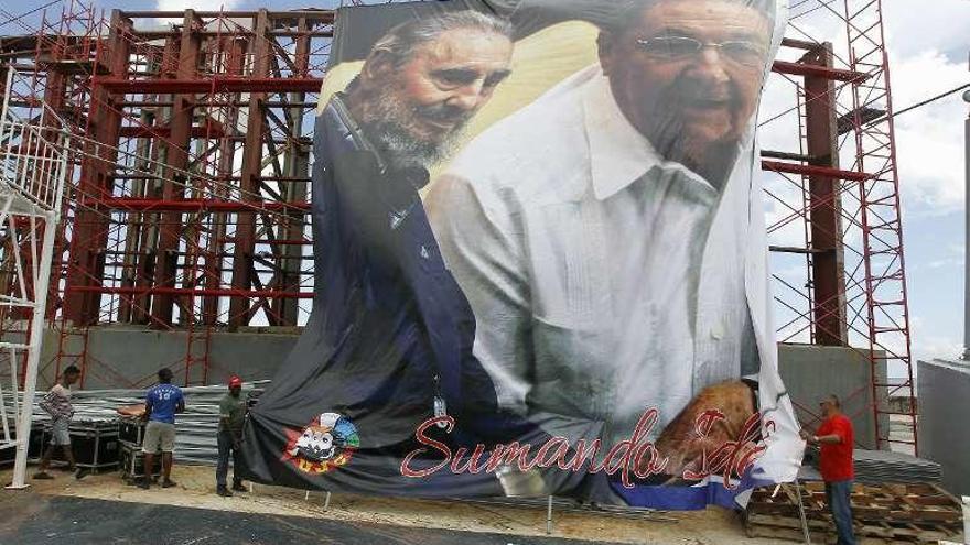Varios obreros despliegan un cartel de Fidel y Raúl Castro. // Efe