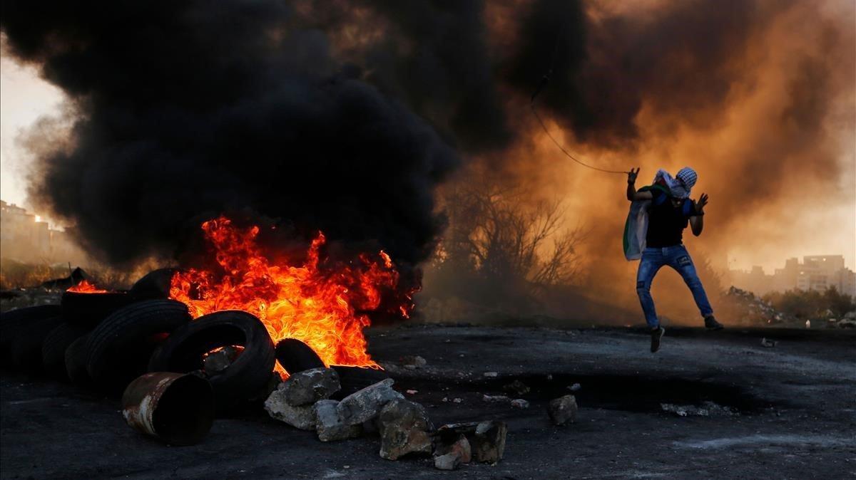 Un joven palestino lanza piedras con una honda, protegido tras el humo.