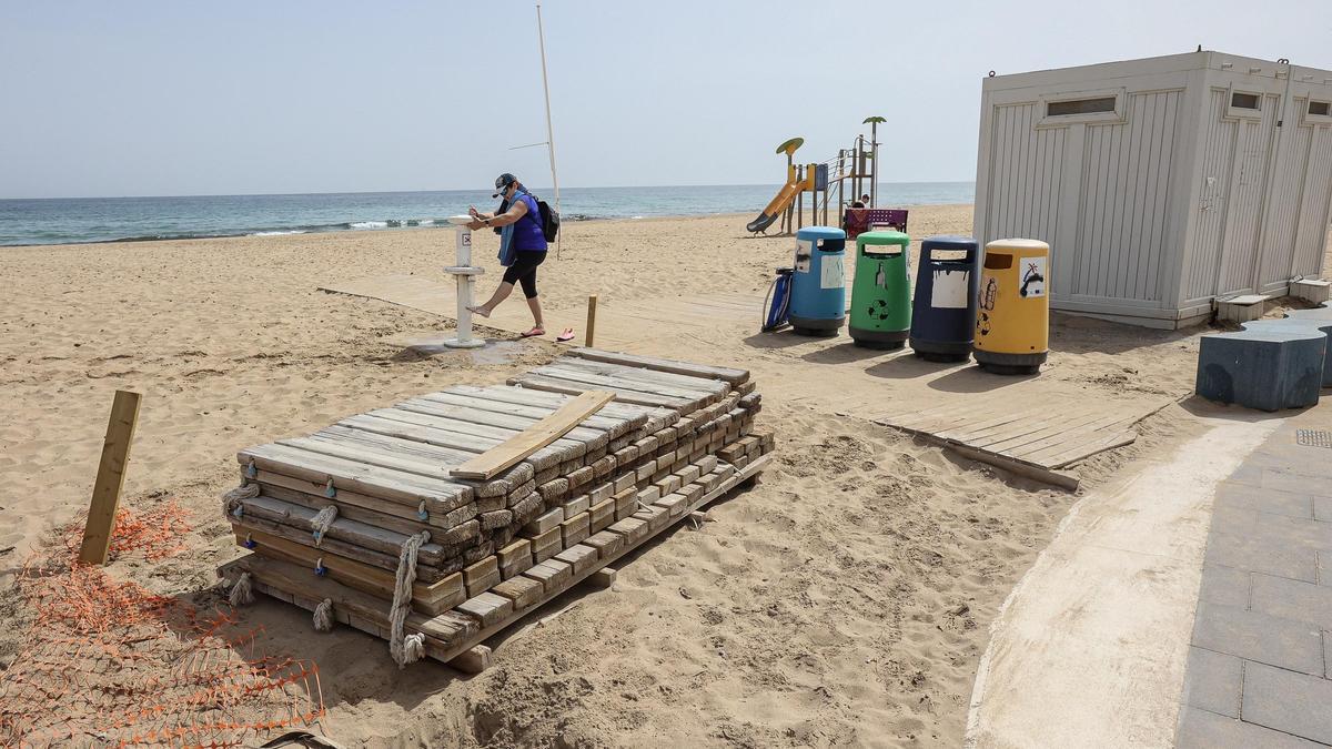 Una usuaria utiliza los lavapiés de la playa de Urbanova con la extensión de las pasarelas de madera pendientes de instalar.