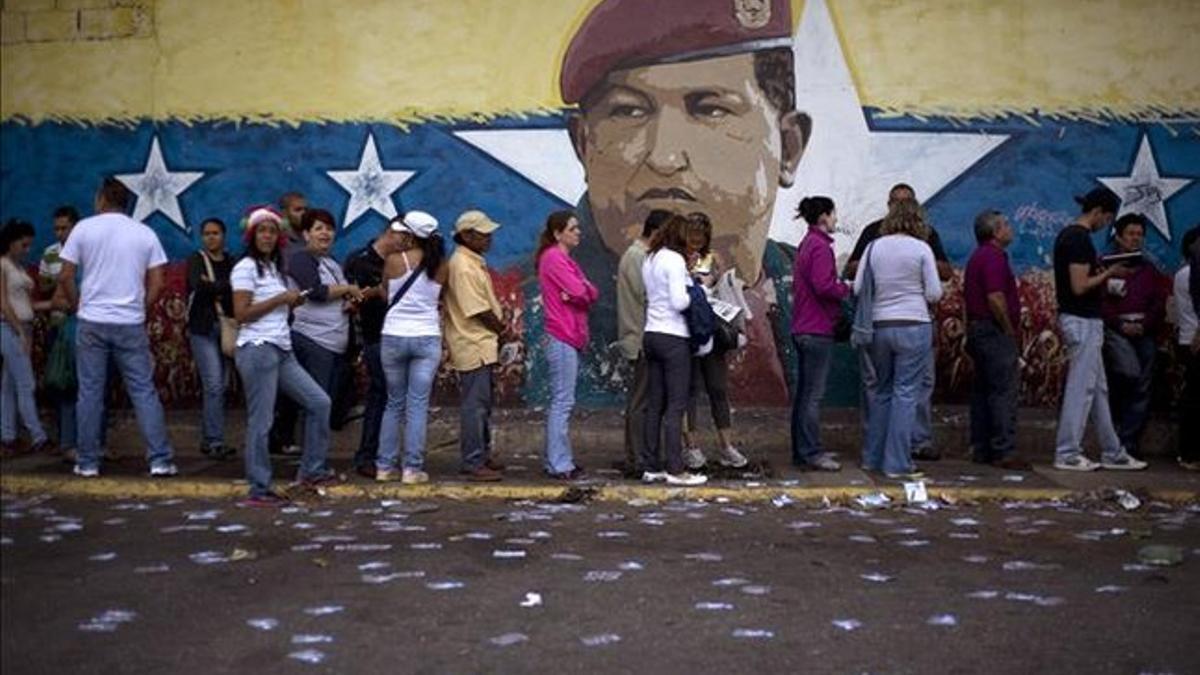 Un grupo de venezolanos hacen cola para votar ante un mural de Hugo Chávez, en Caracas, este domingo.