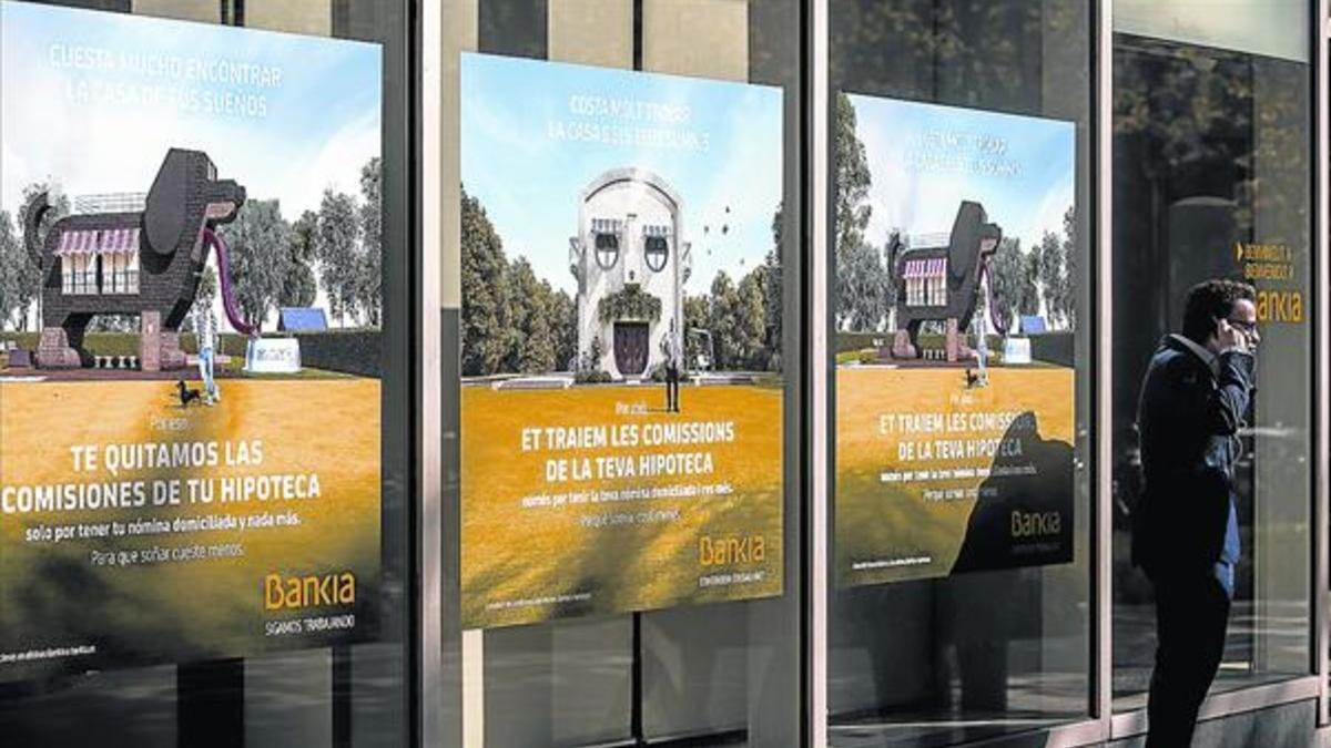 Un hombre, ante una oficina de Bankia, con publicidad sobre sus hipotecas.