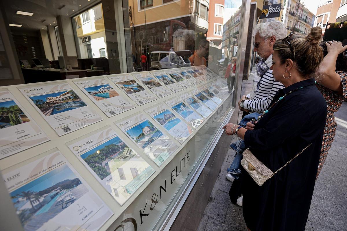 Varias personas miran el escaparate de una inmobiliaria en el centro de Alicante.