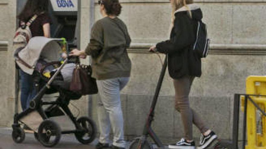 Una chica en patinete circula por una acera.