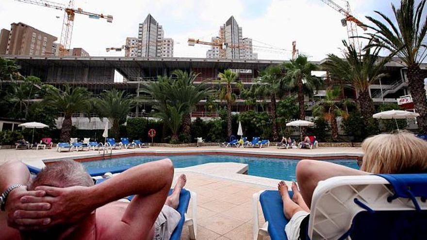 Dos turistas toman el sol en la piscina del hotel Castilla, de la cadena Servigroup, ante la estructura y las grúas del Centro Cultural, cuyas obras llevan meses paradas.