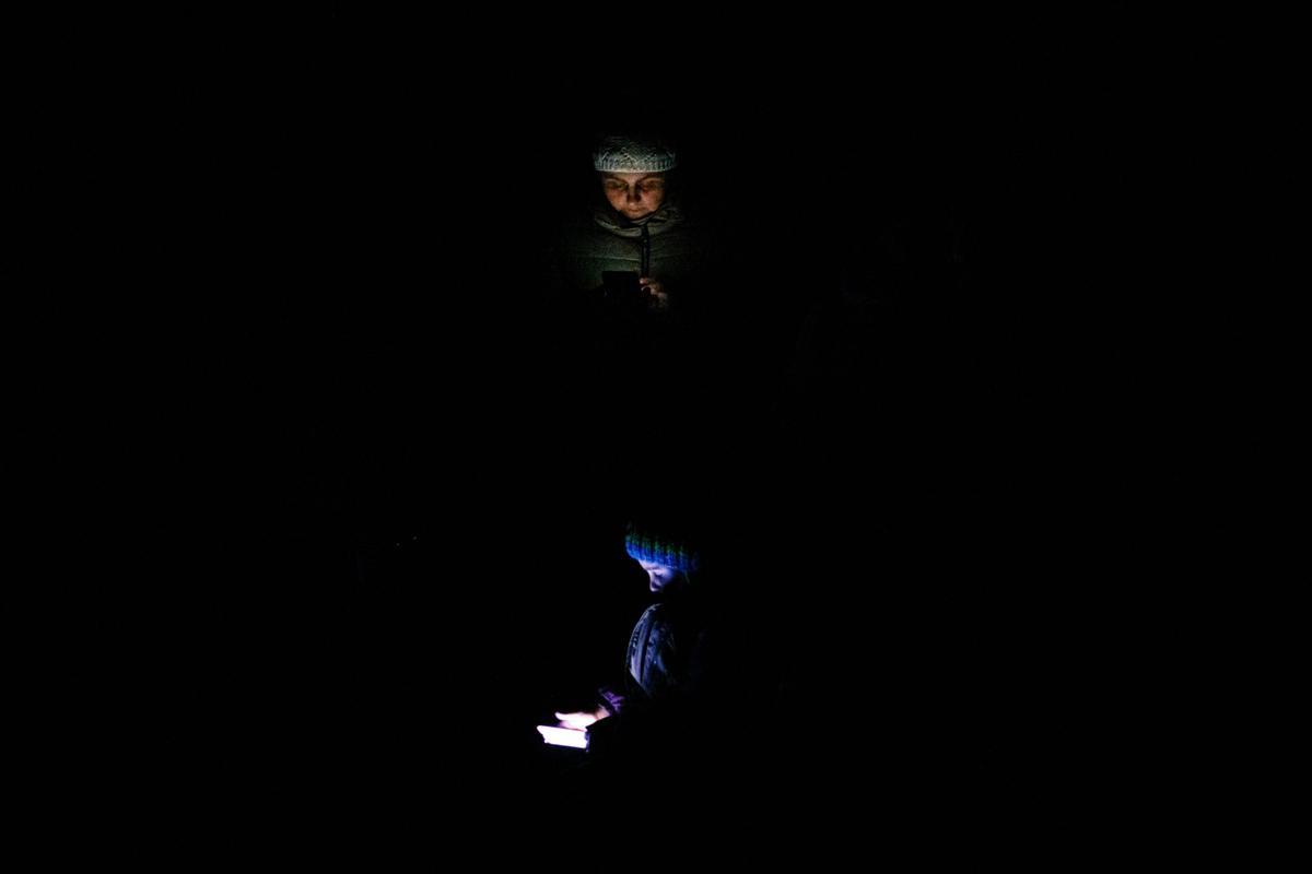 Una mujer y un niño miran sus teléfonos móviles en plena noche, mientras esperan ser evacuados en tren desde Kiev.