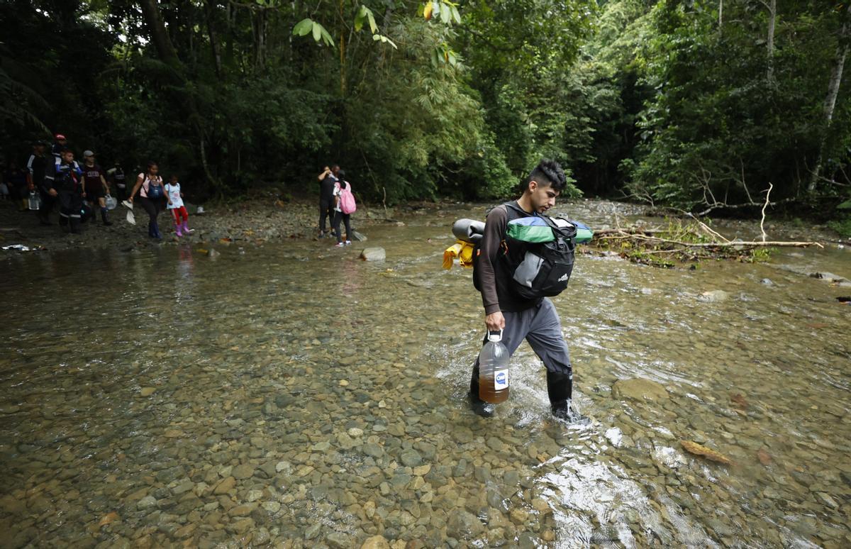 Migrantes cruzan un río de la selva del Darién, a su paso por Colombia, cargados con sus pertenencias.