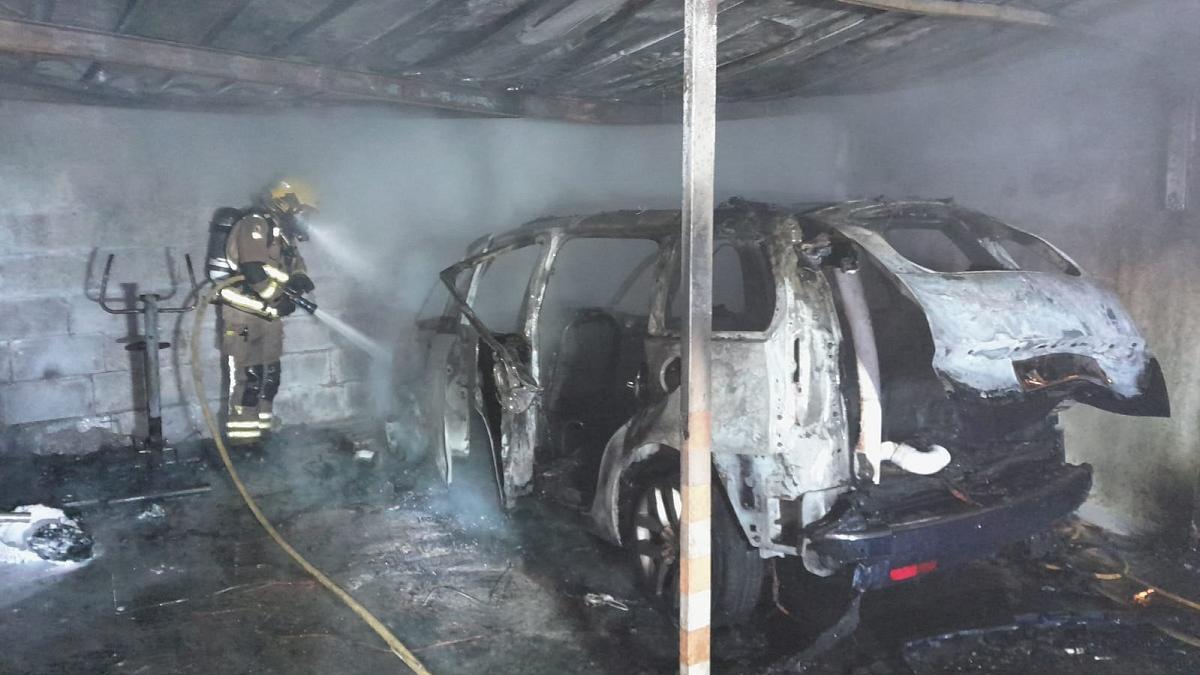 Un bombero actúa sobre el coche quemado en el garaje de la vivienda de Mos