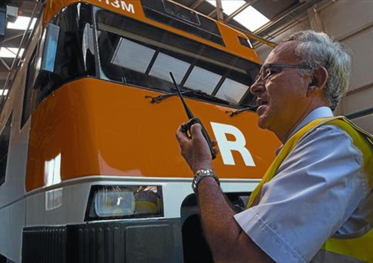 Un treballador dels tallers de Renfe a Vilanova i la Geltrú, davant d’un Rodalies amb el nou logo, al juliol.