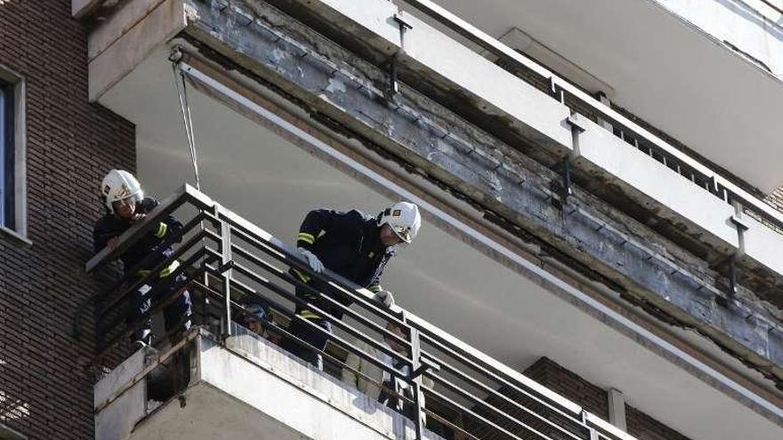 Dos bomberos inspeccionan el balcón que se desprendió.