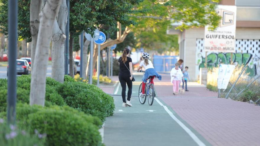 Una chica monta en bicicleta por un carril bici de Murcia mientras que otra se cruza caminando.