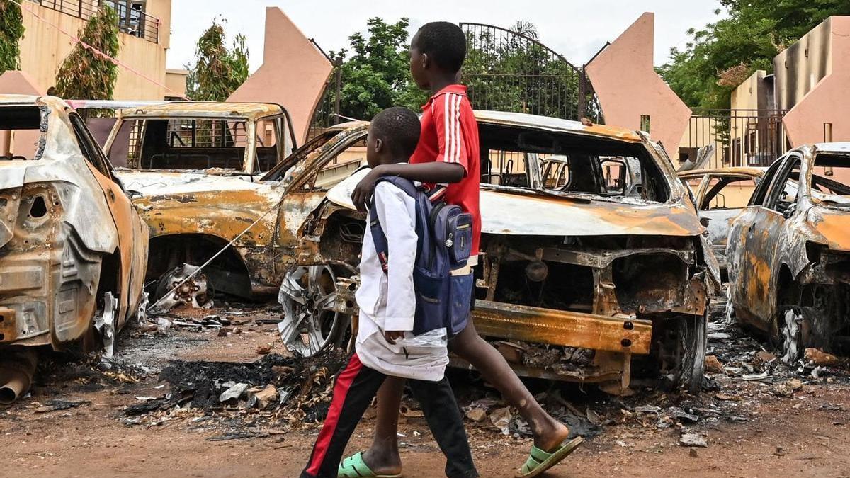 Dos niños pasean frente a un coche incendiado en Níger.