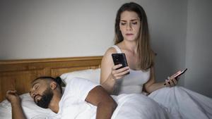 Una mujer revisa el móvil de su pareja mientras éste duerme.