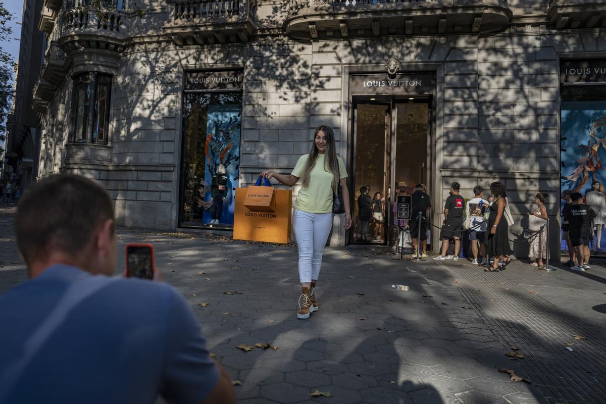 Colas frente a la tienda de Louis Vuitton y, en primer plano, una clienta que se retrata con sus compras.