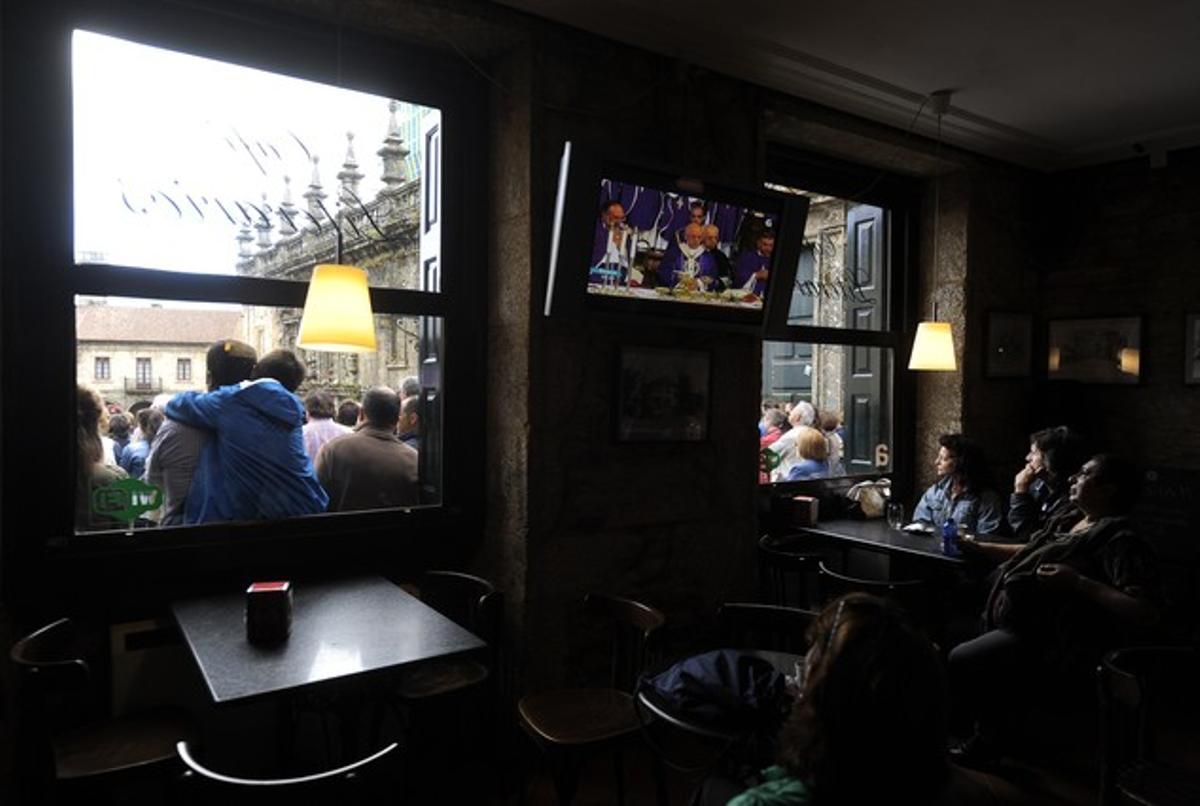 Nombroses persones veuen a través del televisor d’un bar de darrere de la catedral de Santiago el funeral oficial per les 79 víctimes mortals de l’accident de tren del dia 24, aquest dilluns.