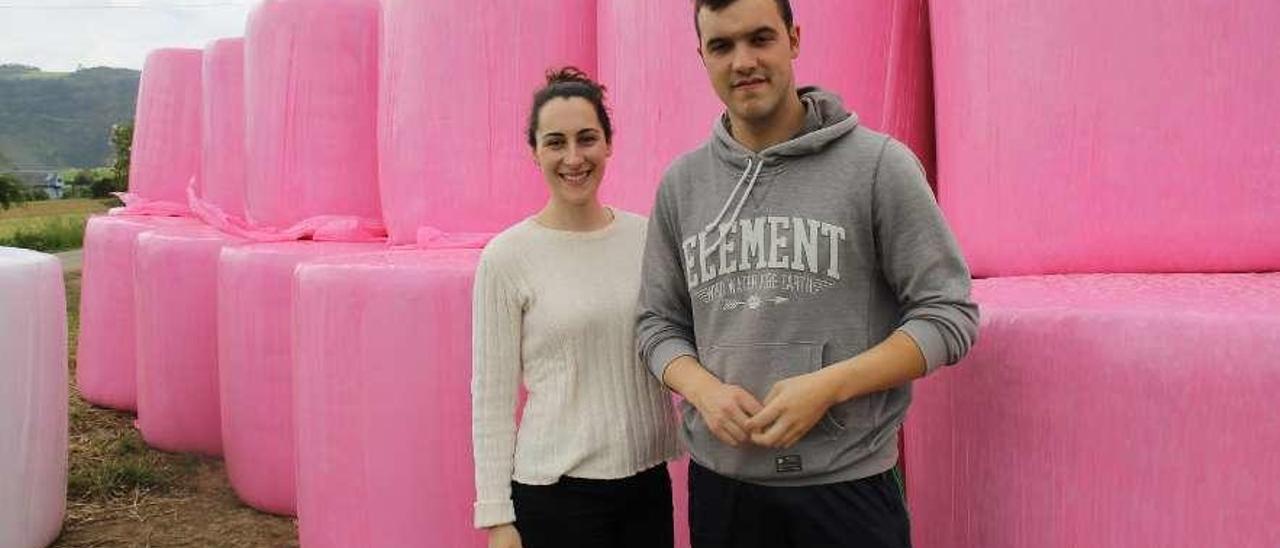 Natalia López e Iván Martínez junto a los rollos de hierba ensilada con plástico rosa, en Villapedre.