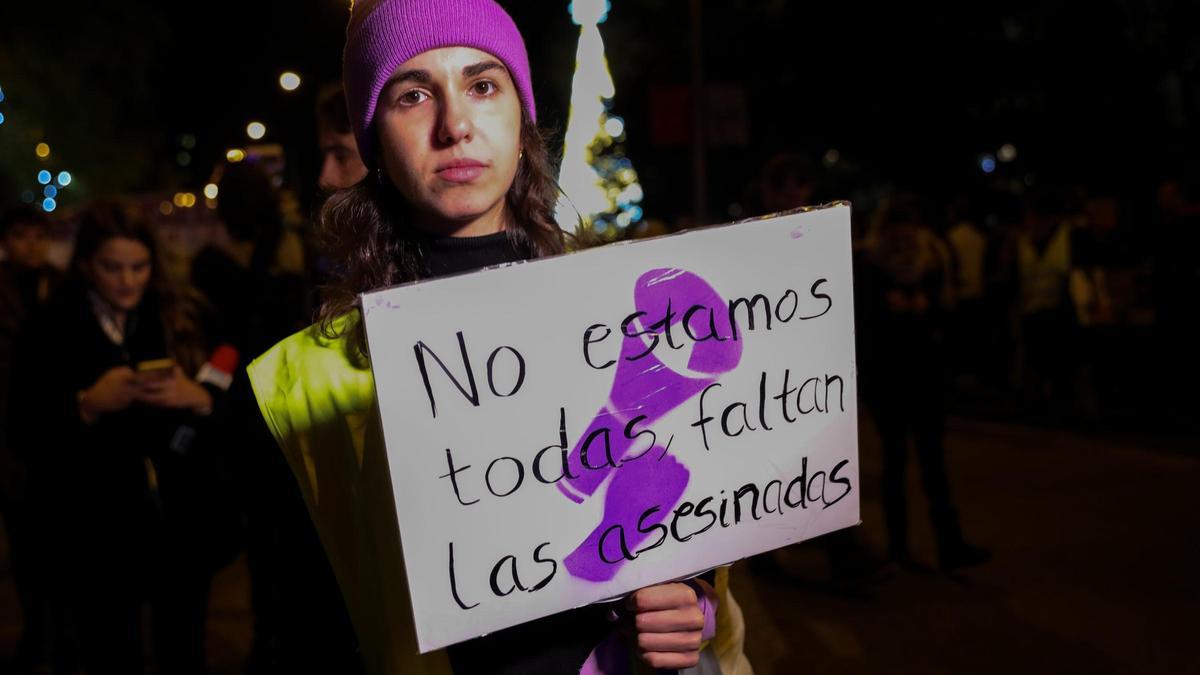 Una mujer con un gorro morado sostiene una pancarta en una protesta.