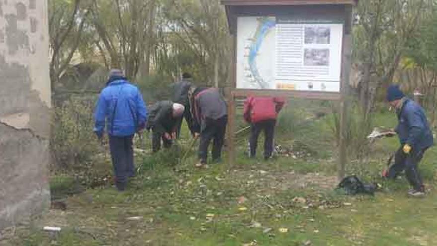 Los voluntarios trabajan en la limpieza de sendero con al Puente de Piedra al fondo.