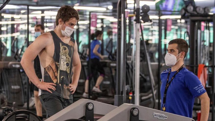 Dos personas se ejercitan con mascarilla en un gimnasio.