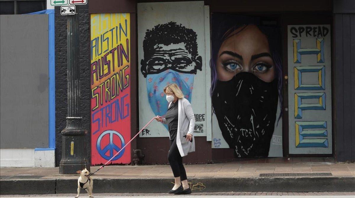 undefined53045334 a woman wears a mask as she walks her dog past a boarded up 200407221706