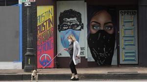 undefined53045334 a woman wears a mask as she walks her dog past a boarded up 200407221706