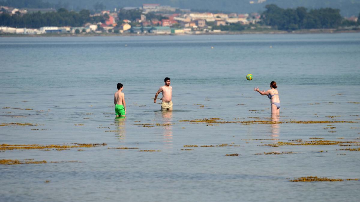 Tres personas juegan en el agua de una playa de A Illa