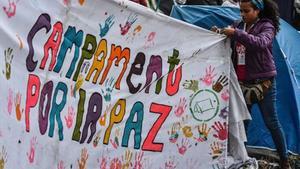 Una joven ayuda a colocar una pancarta a favor del acuerdo de paz en una acampada en Bogotá.