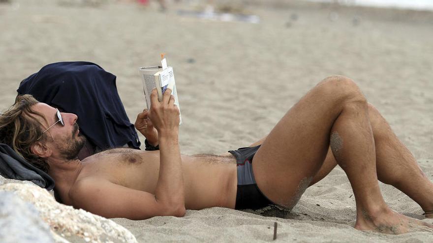 Un turista lee un libro en la playa de El Bajondillo, en Torremolinos.