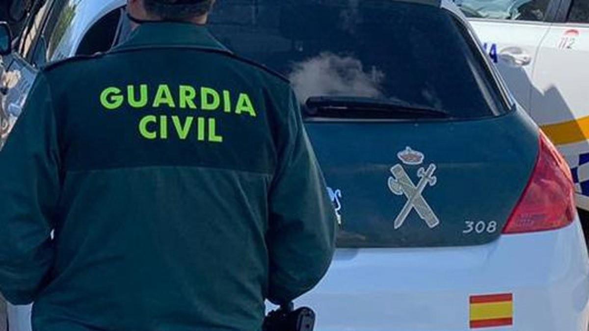 Archivo - Un agente de la Guardia Civil junto a un vehículo oficial. Archivo.
