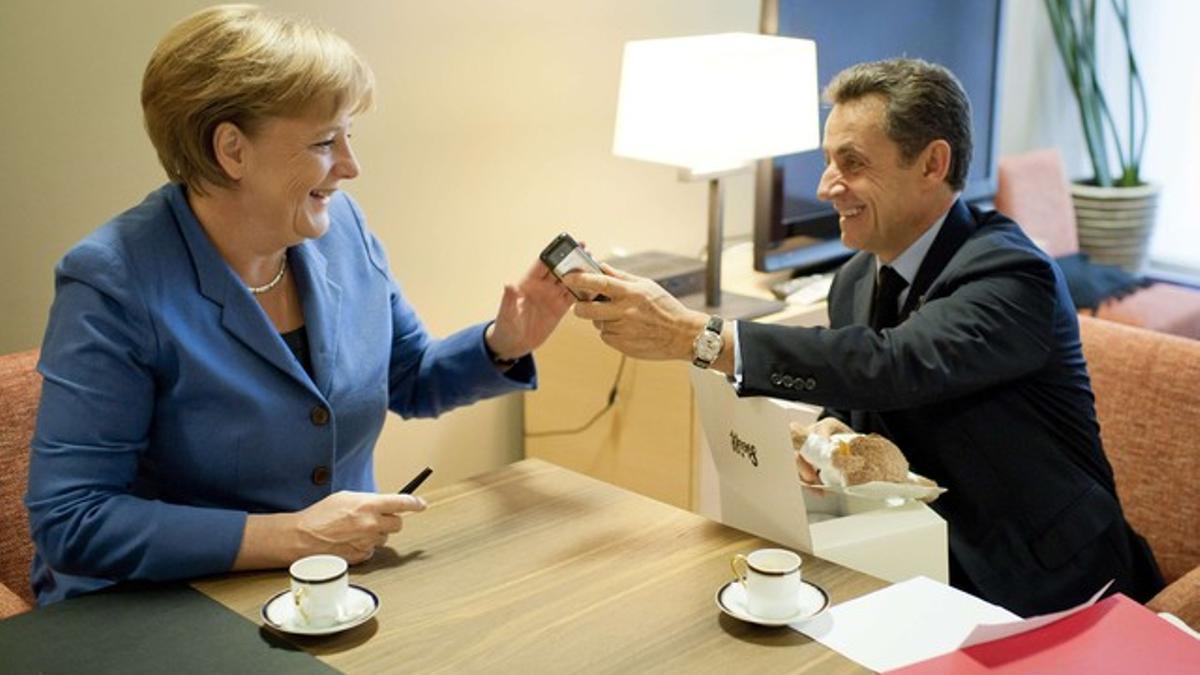 Angela Merkel regala a Nicolas Sarkozy un peluche para su hija recién nacida y él le pasa su móvil para que felicite a su mujer, Carla Bruni, el domingo, en Bruselas.