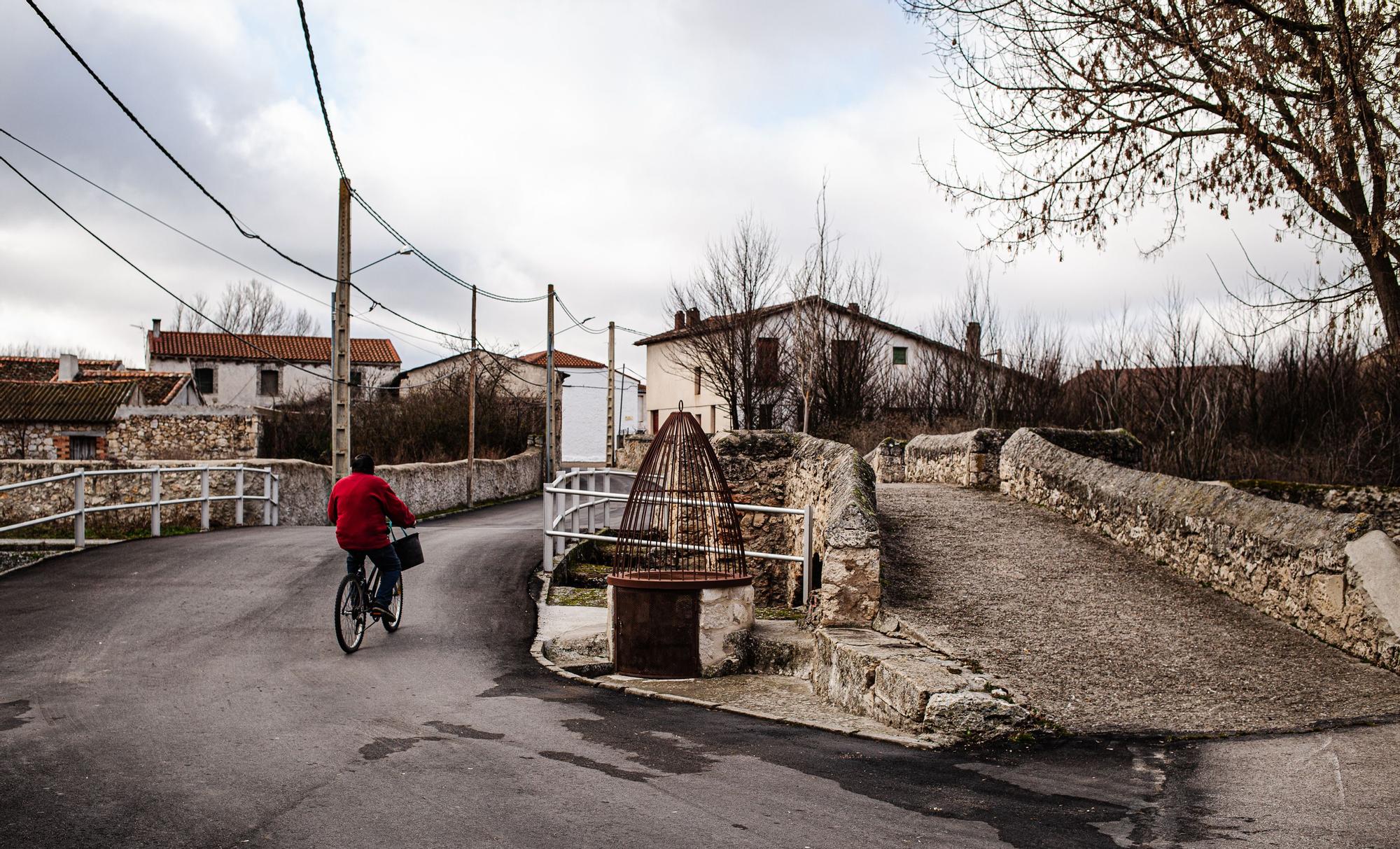 Un vecino de Fuente Olmo de Fuentidueña pasa con su bicicleta por el puente romano de la localidad.