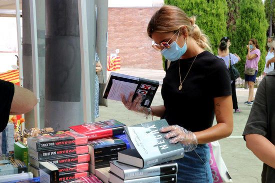 Una noia amb mascareta i guants consultant llibres d'una parada de Sitges.